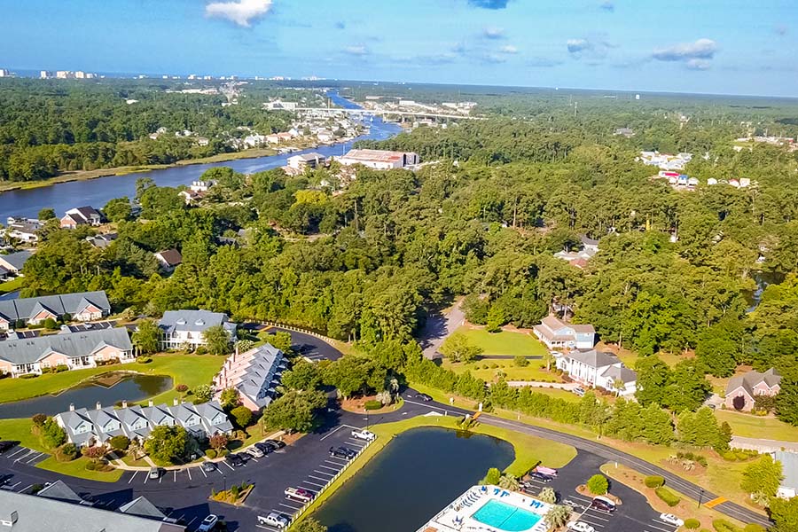 Little River, SC - Aerial View of a Group of Townhomes With Many Trees and a Large River on a Sunny Day