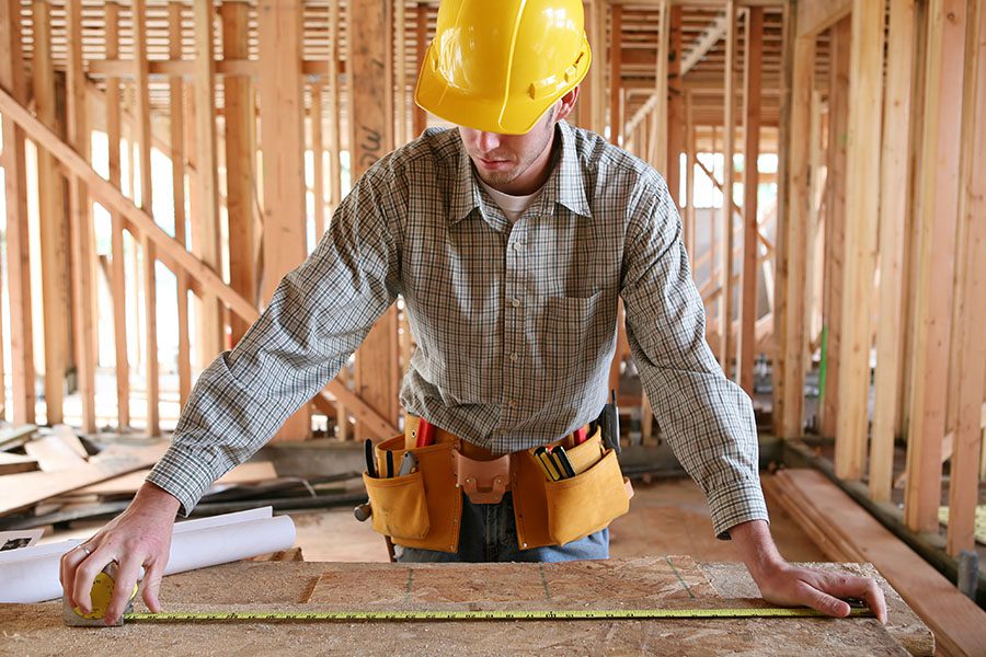 Specialized Business Insurance - A Contractor Wearing a Yellow Hardhat is Using a Tape Measure to Measure a Table at a Home Construction Site